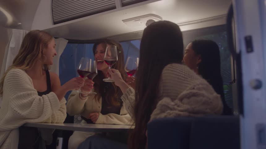 Four women toasting with wine glasses inside a trailer
