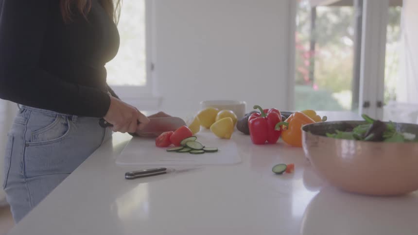A woman is cutting fresh vegetables there are some red and yellow bell paper on table