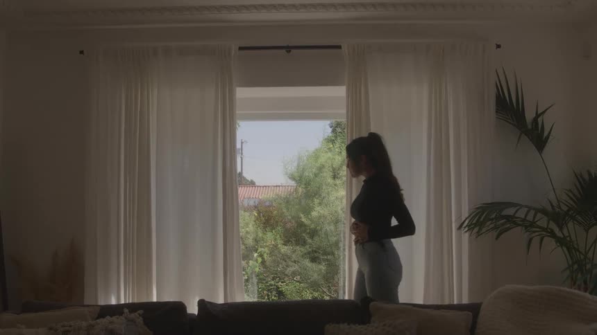 Woman standing and looking outside through a glass door with white curtains