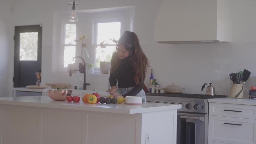 The woman is cutting food and smiling in the kitchen
