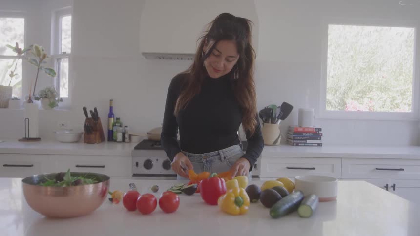 The woman is cutting an orange pepper