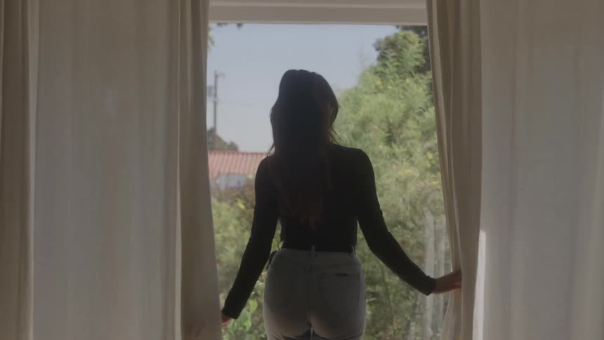 Woman spreading a curtain to reveal tree lines outside through the window at midday