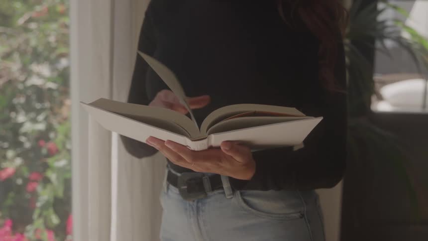 Woman standing leafing through a book while standing next to a glass door