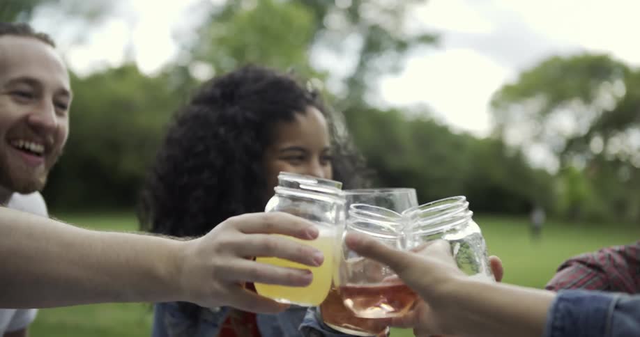 A group of people sitting outside on the ground laughing and toasting