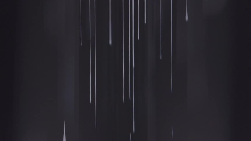 Droplets of white paint dripping against a black background