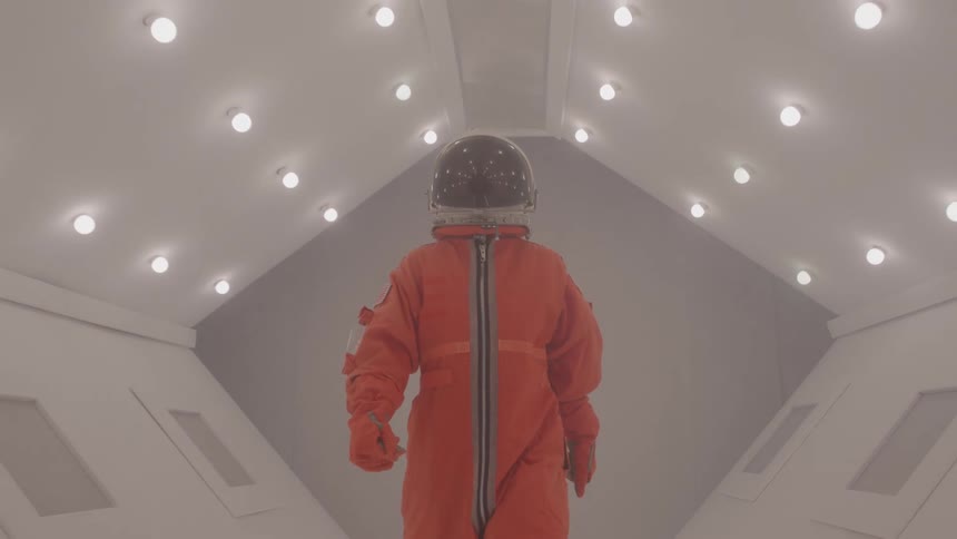 Person wearing an orange spacesuit walking through a lit corridor