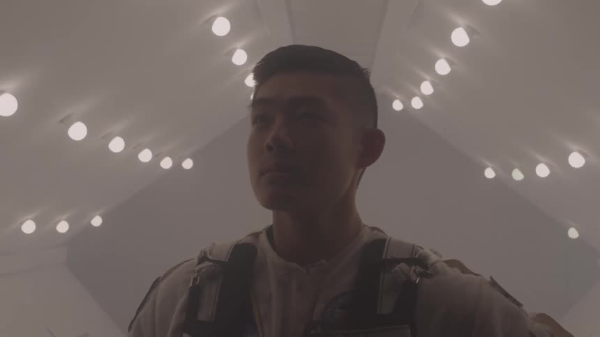 Man in a white spacesuit inside a room lit by multiple ceiling lights