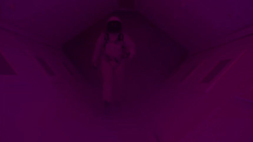 In this short clip a person in a white spacesuit walks through a dark narrow hallway lit by an eerie pulsing red light the camera follows closely from behind creating a tense suspenseful atmosphere as the figure moves toward the viewer