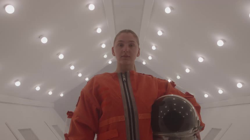 Astronaut in an orange suit holds the helmet under the arm