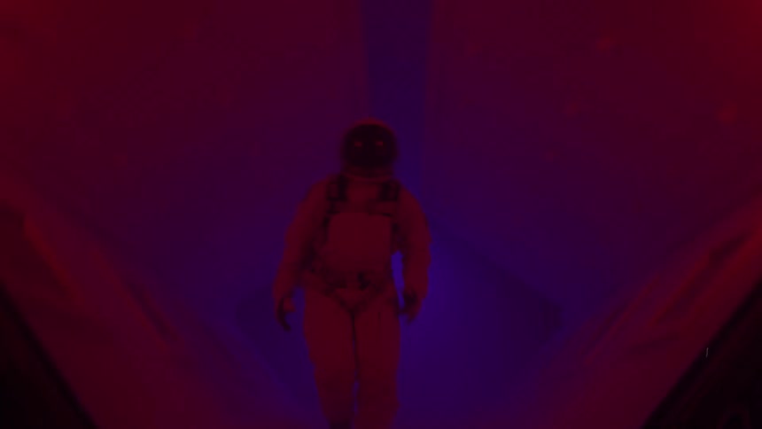Person wearing a spacesuit runs down a hallway lit by emergency lights