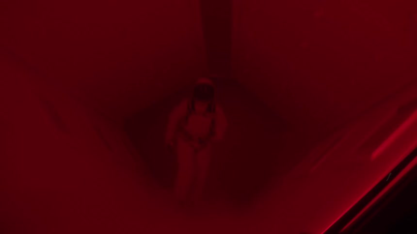 Person wearing a spacesuit runs down a corridor lit by lights