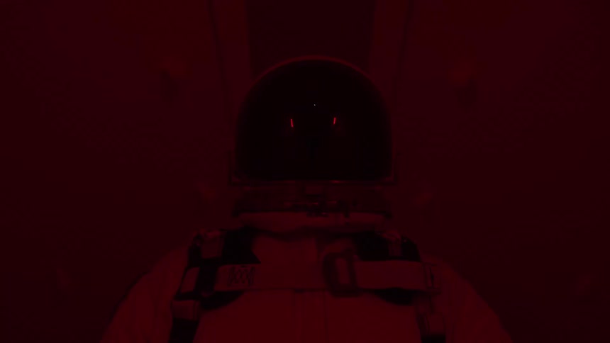 Person wearing a spacesuit and helmet inside a spaceship with a dark atmosphere illuminated by red ambient light
