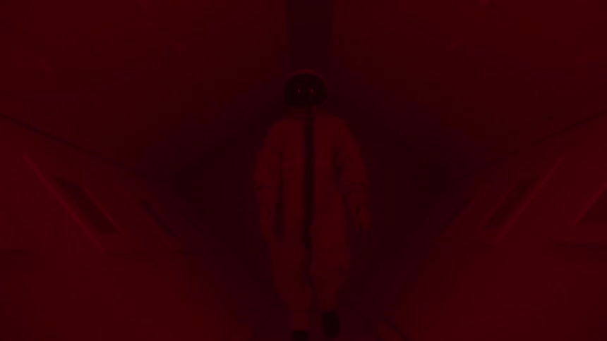 A person in a spacesuit and helmet walking inside a spaceship under red flickering emergency lights