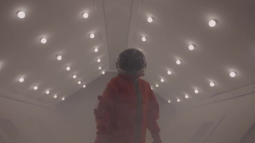 Astronaut in orange suit walks through corridor filled with mist