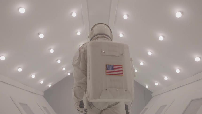 Person in spacesuit walking down a white lit hallway