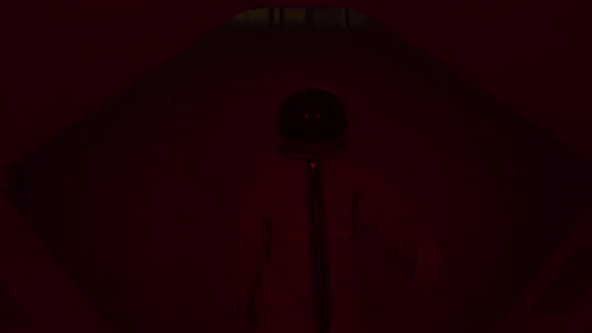 Astronaut in orange suit walks through corridor lit by purple light