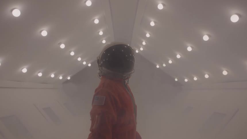 Astronaut in orange suit looks at illuminated ceiling in a misty room