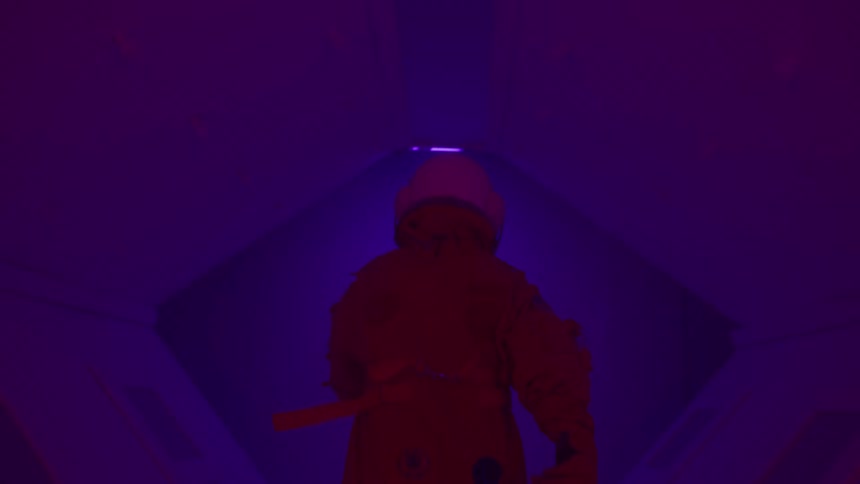 Person in spacesuit walking down a hallway with flashing red lights