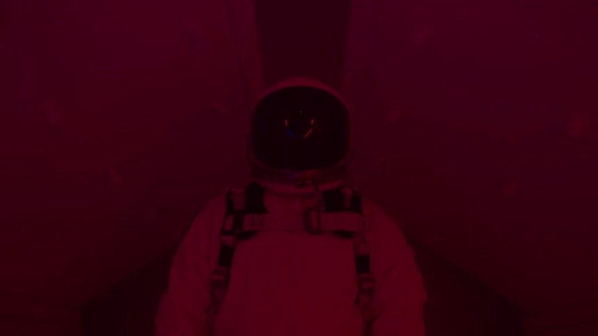 Astronaut in white suit stands in corridor lit by purple light