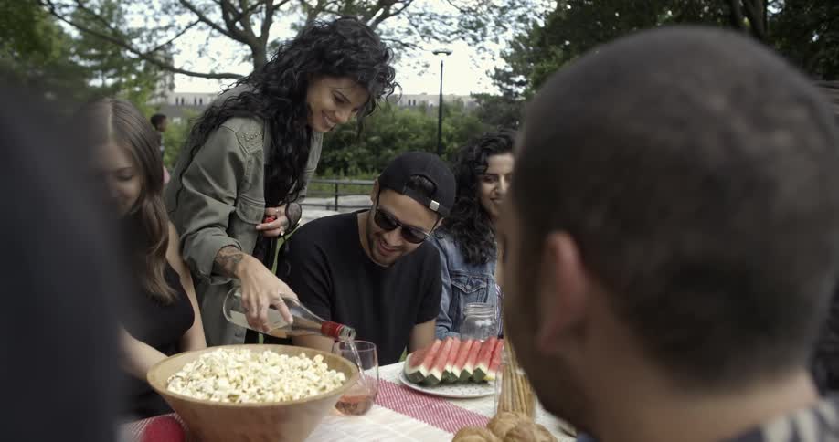 A woman pours drinks for people at a outdoor picnic