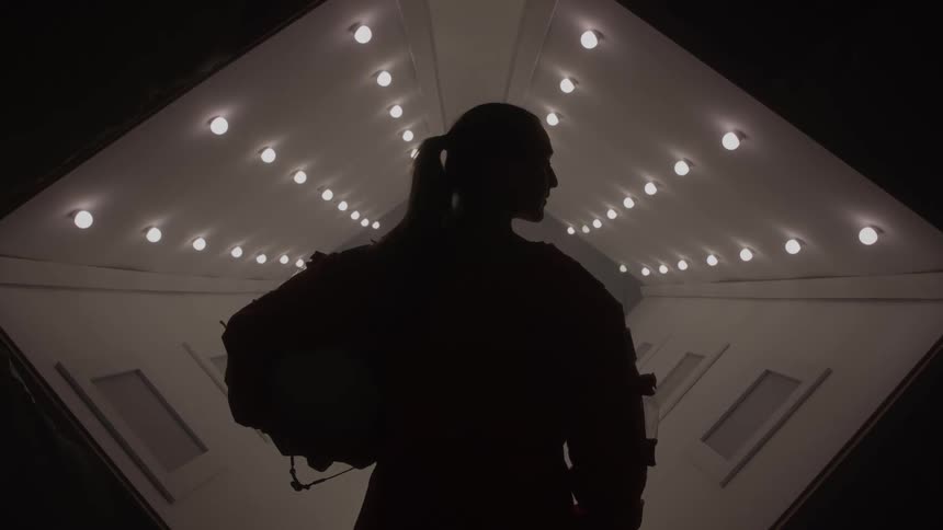 Silhouette of astronaut in orange suit facing illuminated ceiling