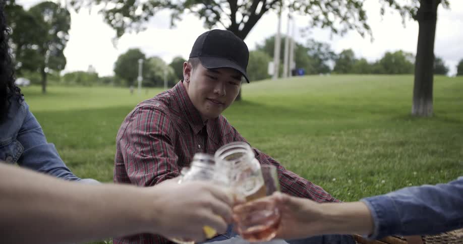 A group of people sitting outside on the ground drinking from mason jars