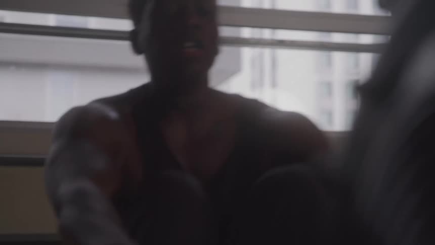 A man in a black tank top works out intensely swinging heavy ropes with focused determination