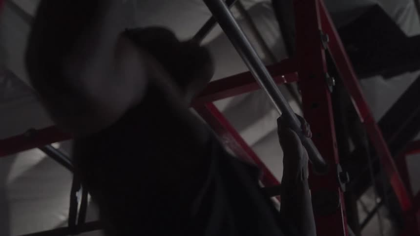 In this clip a person is doing a pullup with their hands gripping a metal bar the lighting is dim casting the person in shadow but their effort is evident as they pull their body weight up