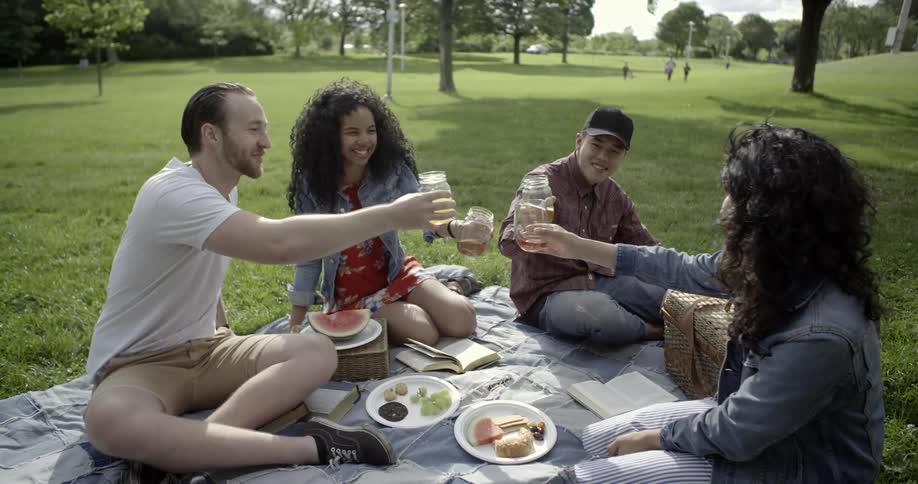 Group of men and women clinking jars together and drinking at a picnic