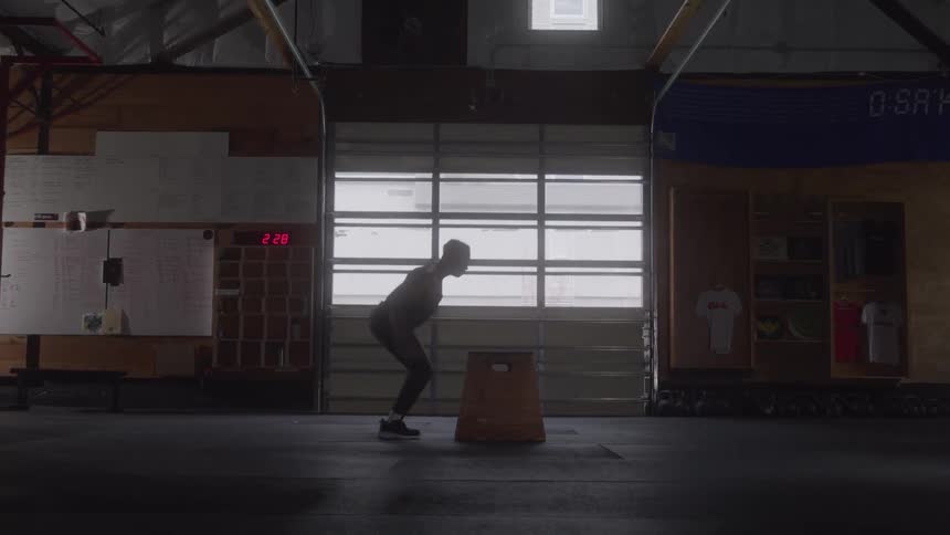 Man prepares to jump onto a plyometric box inside a gym