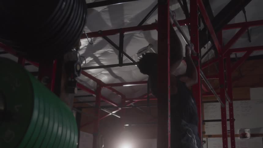 A young black man performing chin ups in a fitness room