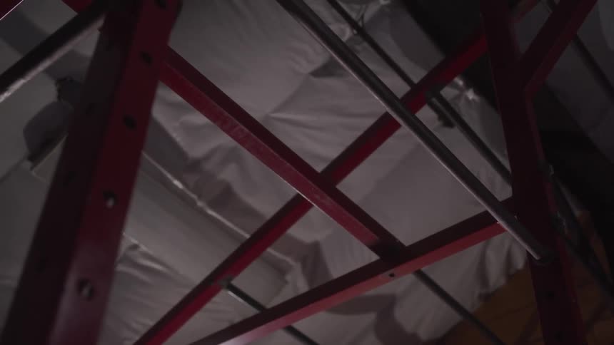 A red metal gym frame with a pullup bar is seen from below against padded ceiling insulation