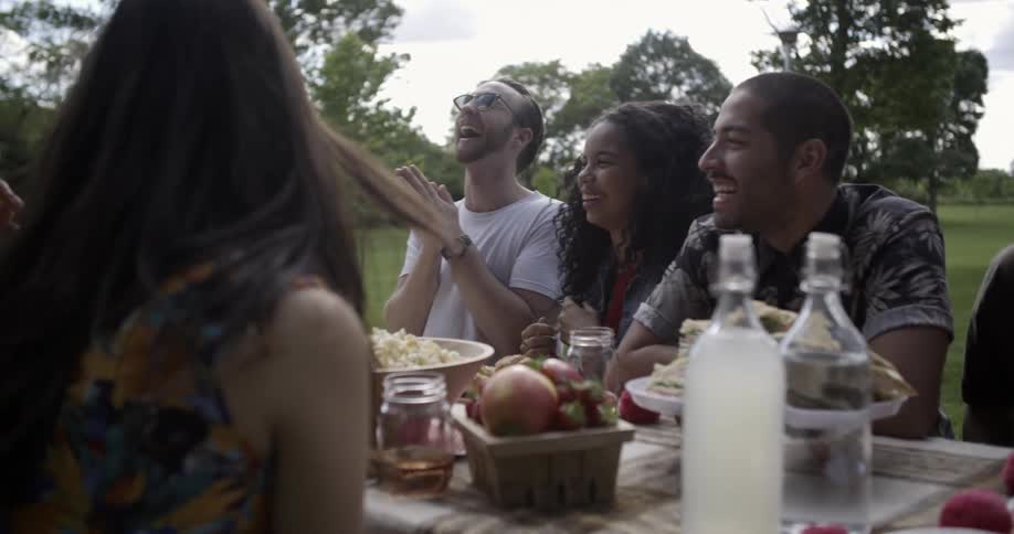 A group of people sit at a table outside talking and eating