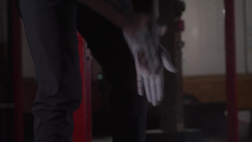 Man in the gym rubbing white powder on his palms preparing to lift a heavy weight