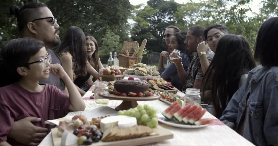 Group of people sitting at a picnic table with food on it outside