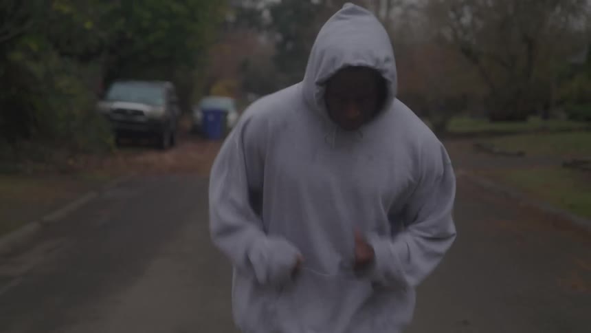 A person in gray sweats runs along a road while wearing a hoodie