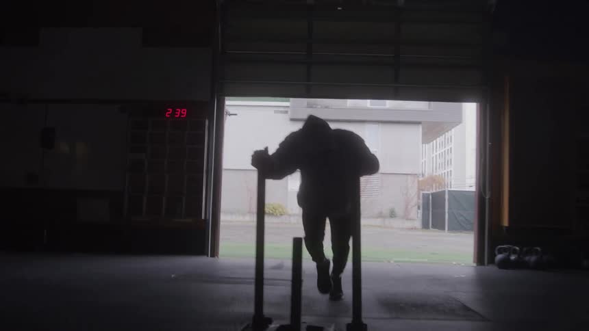 The man leans forward pushing the cart with weights fast