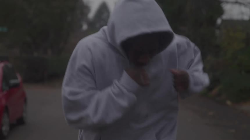 Man wearing a hoodie shadow boxing while jogging down a street at sunrise