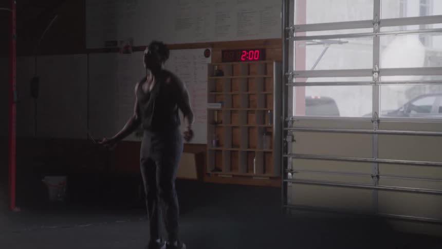 A black man is jumping rope in a dimly lit room
