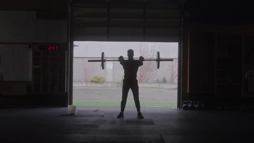 A young black man lifting gym weights in a fitness room during daytime
