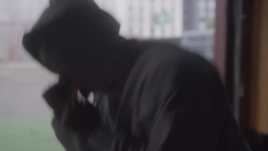 Man wearing a hoodie shadow boxing indoors beside a gym window at midday