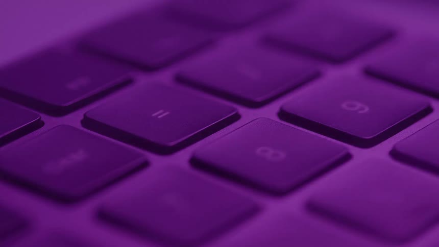 Extreme close up of a computer keyboard in a room lit with multiple colours