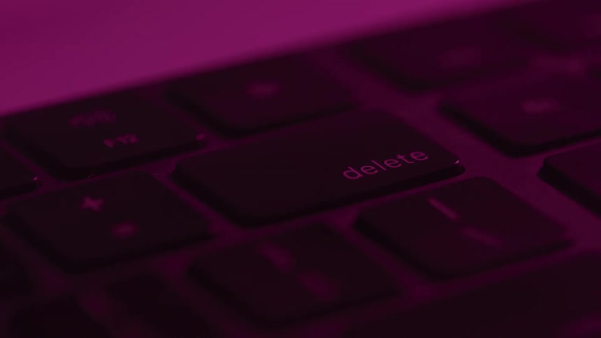A close view of a black keyboard with a finger pressing the delete key as the lighting changes colors from blue to red to purple