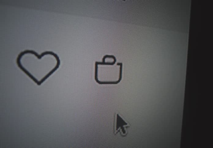 A close view of a computer screen shows a mouse cursor moving towards a shopping cart icon next to a heart icon with visible pixels on the screen