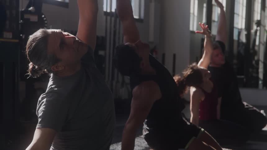 A group of people on their knees on a gym with their arms stretched high rotating their wrists
