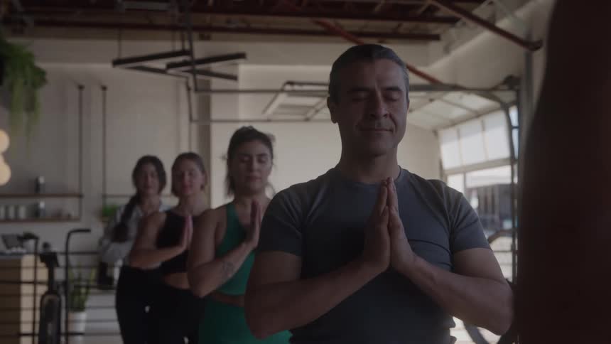 Group of people practice yoga in a studio with hands joined in prayer position