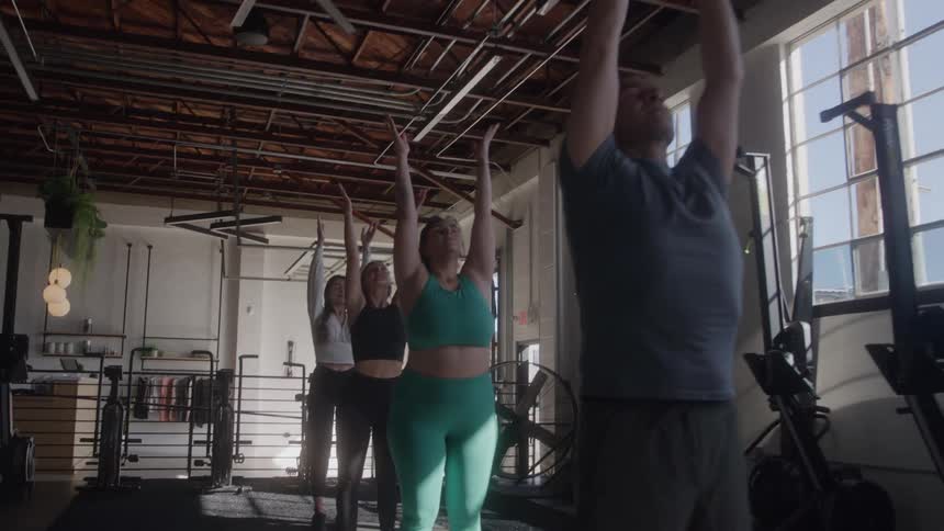 Group of people stretch with arms raised in a studio lit by natural light