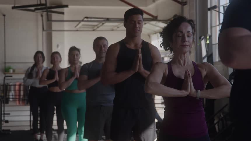 The video shows a diverse group of people participating in a yoga class they are all standing and holding a prayer pose with their hands pressed together at their chests