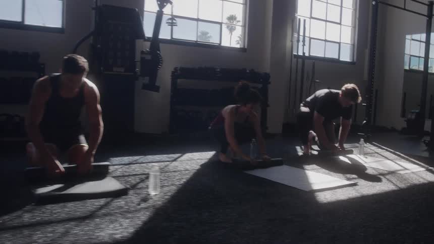 People are rolling up yoga mats in a sunlit gym after a class