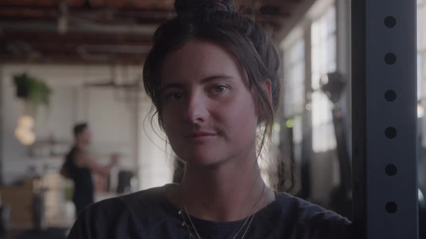 A woman stands in a gym looking into the camera with a calm expression